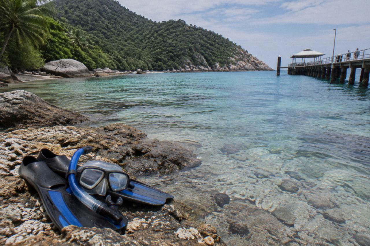 Calm turquoise water over coral reef beside a rainforest covered island shoreline