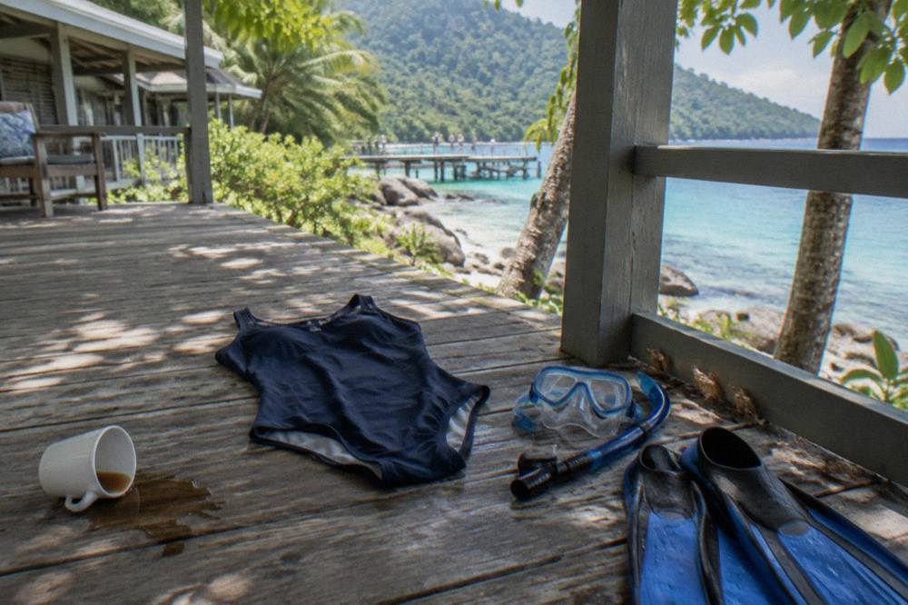 A full body lycra stinger suit laid out on a wooden deck beside snorkel fins and a mask