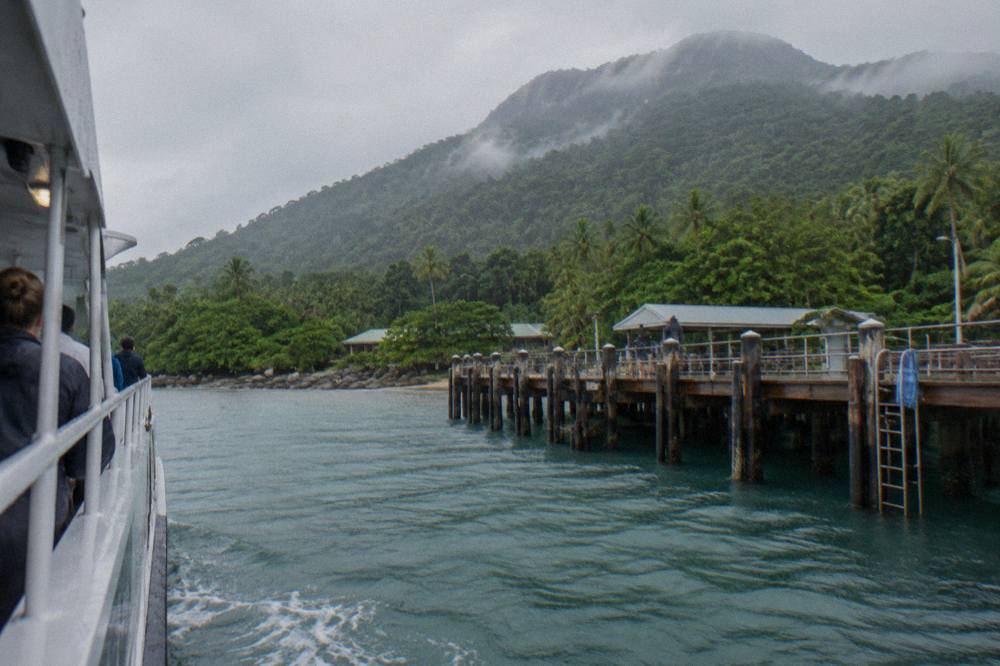 A passenger ferry approaching a wooden jetty on a green tropical island in calm blue water