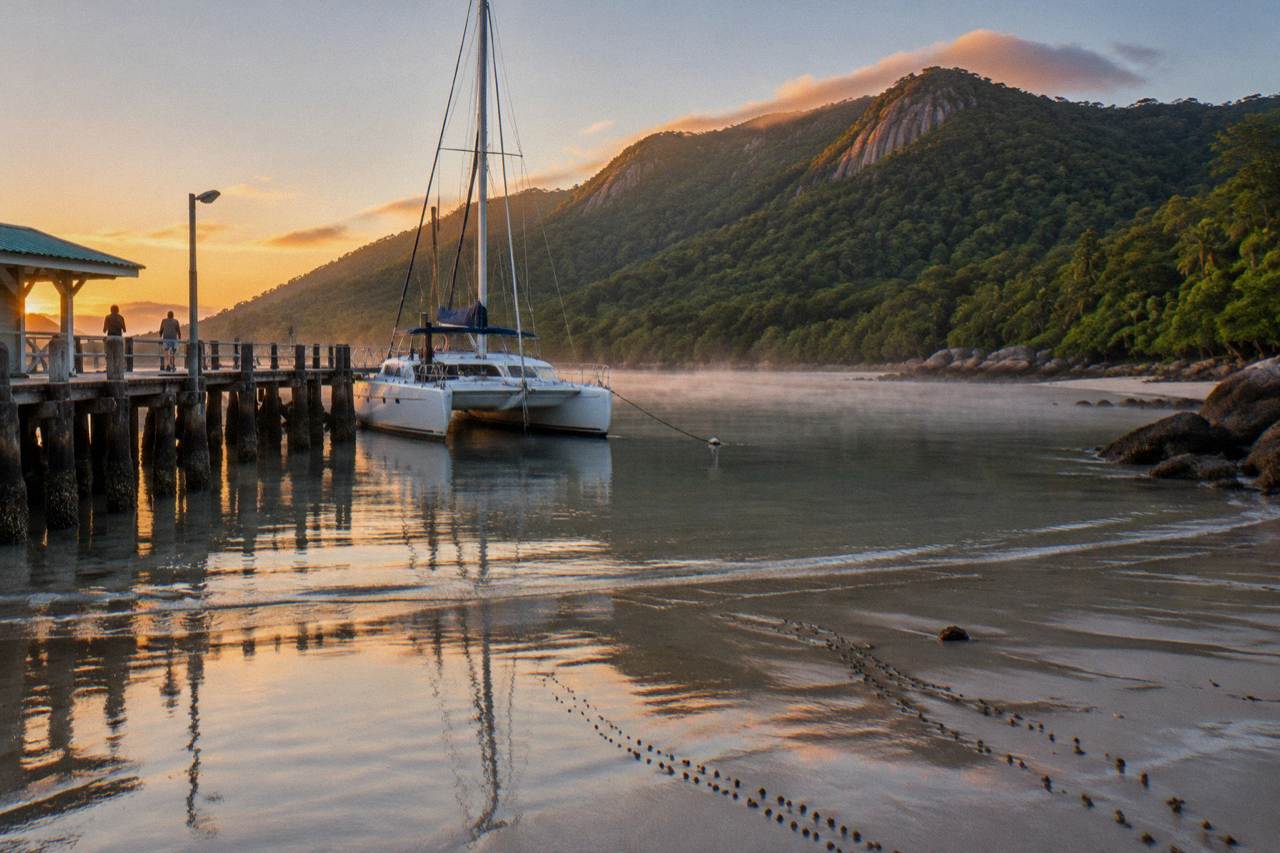 A fast catamaran ferry moored at a tropical island jetty surrounded by clear turquoise water and forested hills