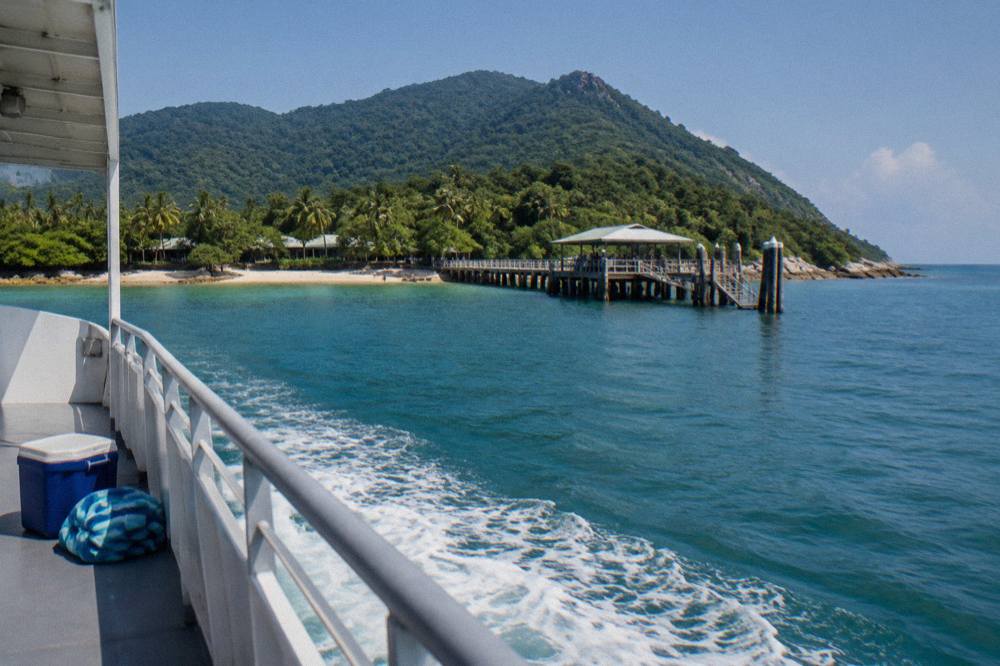 A passenger ferry crossing calm blue water toward a green island coastline