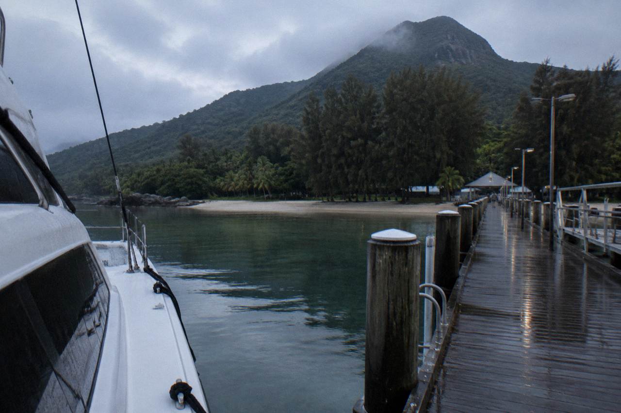 A fast catamaran ferry moored at a tropical island jetty with rainforest covered hills behind