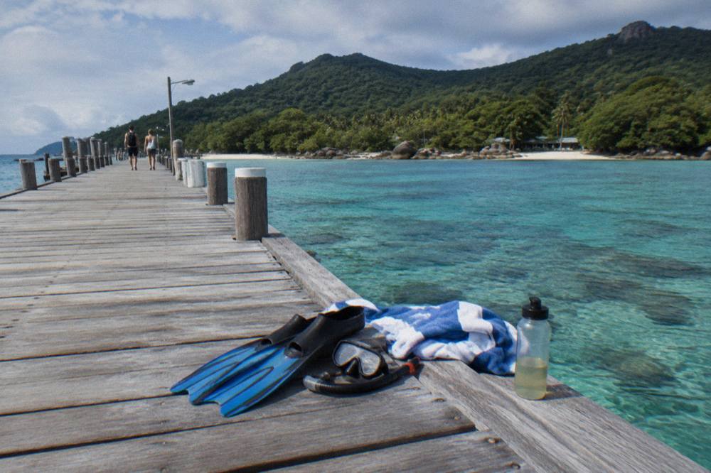 Snorkel mask and fins resting on a wooden jetty beside clear shallow water