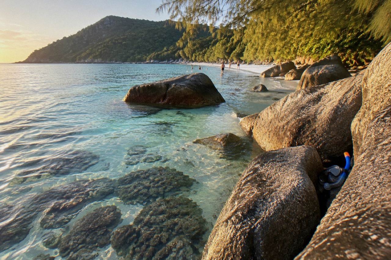 Calm turquoise water over coral reef close to a granite boulder shoreline