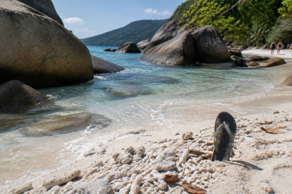 White coral sand beach with clear green water and granite boulders along the shoreline