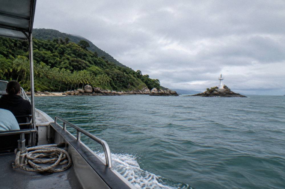 A small tour boat cruising near a wooded tropical island shoreline