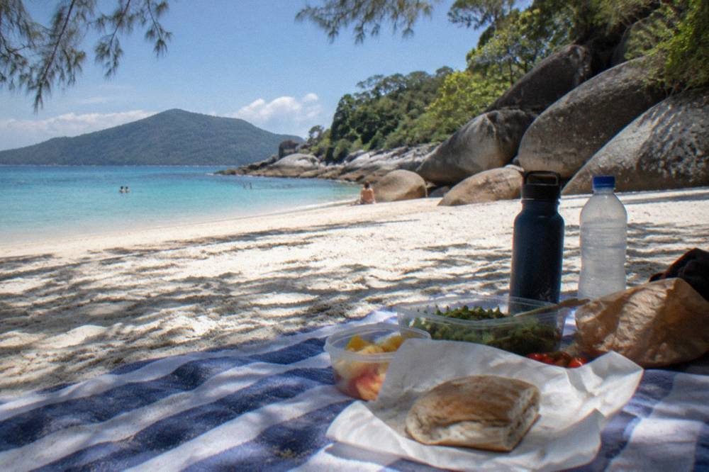 A picnic lunch laid out on a towel on a coral sand beach