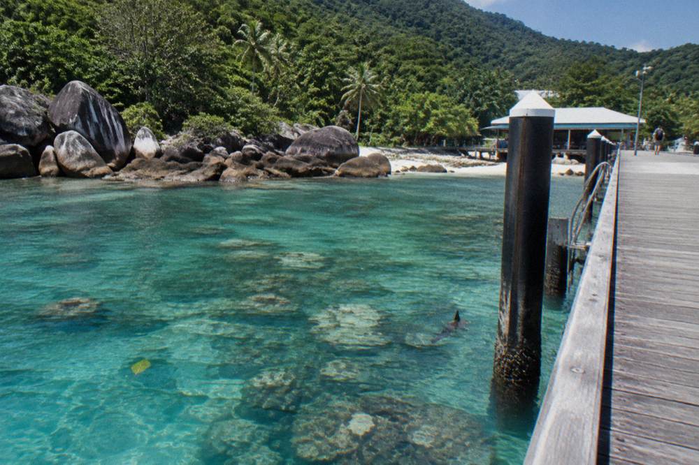 Clear shallow water over coral reef beside a granite boulder shoreline at midday