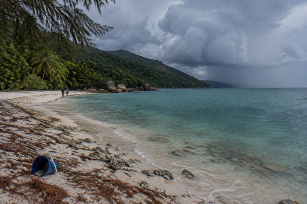 Dark monsoon clouds building over rainforest slopes above a sheltered tropical bay