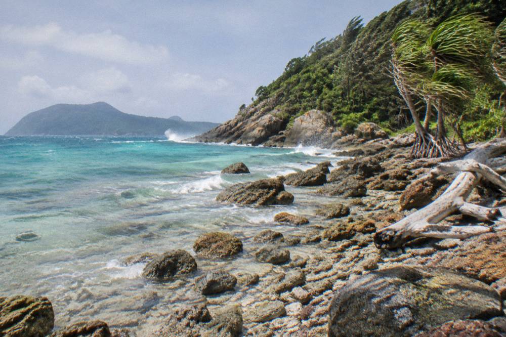 Turquoise shallows over coral beside a tropical island shoreline with rocky headland