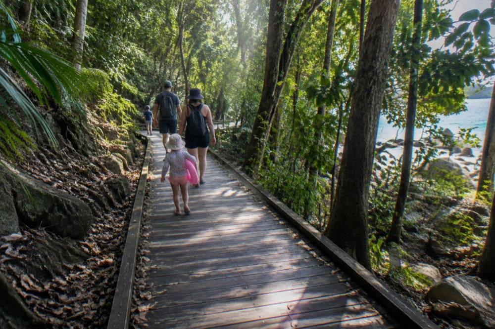 Family walking a shaded rainforest boardwalk track on a tropical island