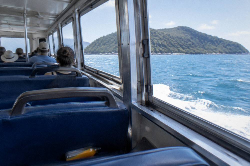 Ferry cabin interior with passengers seated looking out over blue sea toward an island