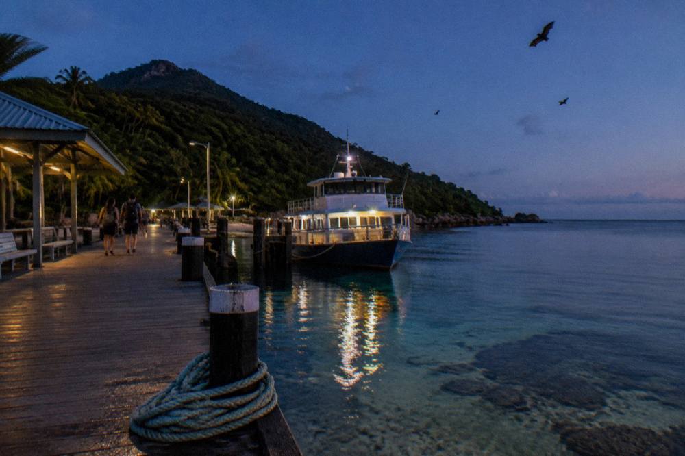 A passenger ferry moored at a tropical island jetty beside clear shallow water