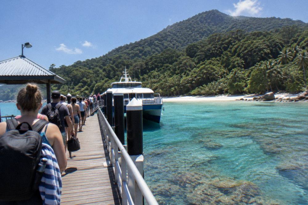 Fast ferry tied at an island jetty with passengers boarding under a blue sky
