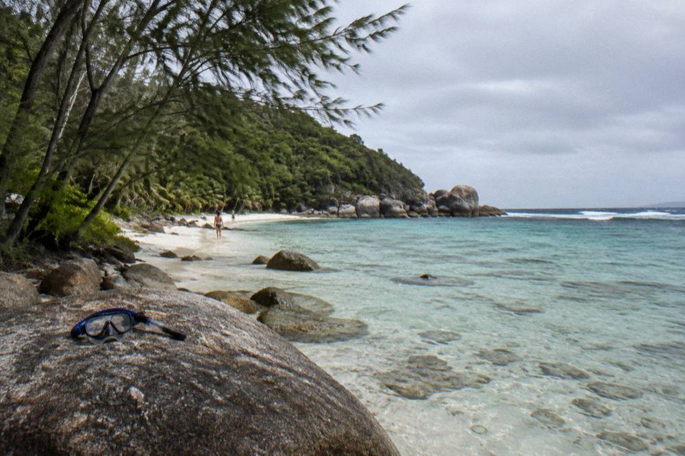 A sheltered tropical beach with clear shallow water over coral and rocky headland