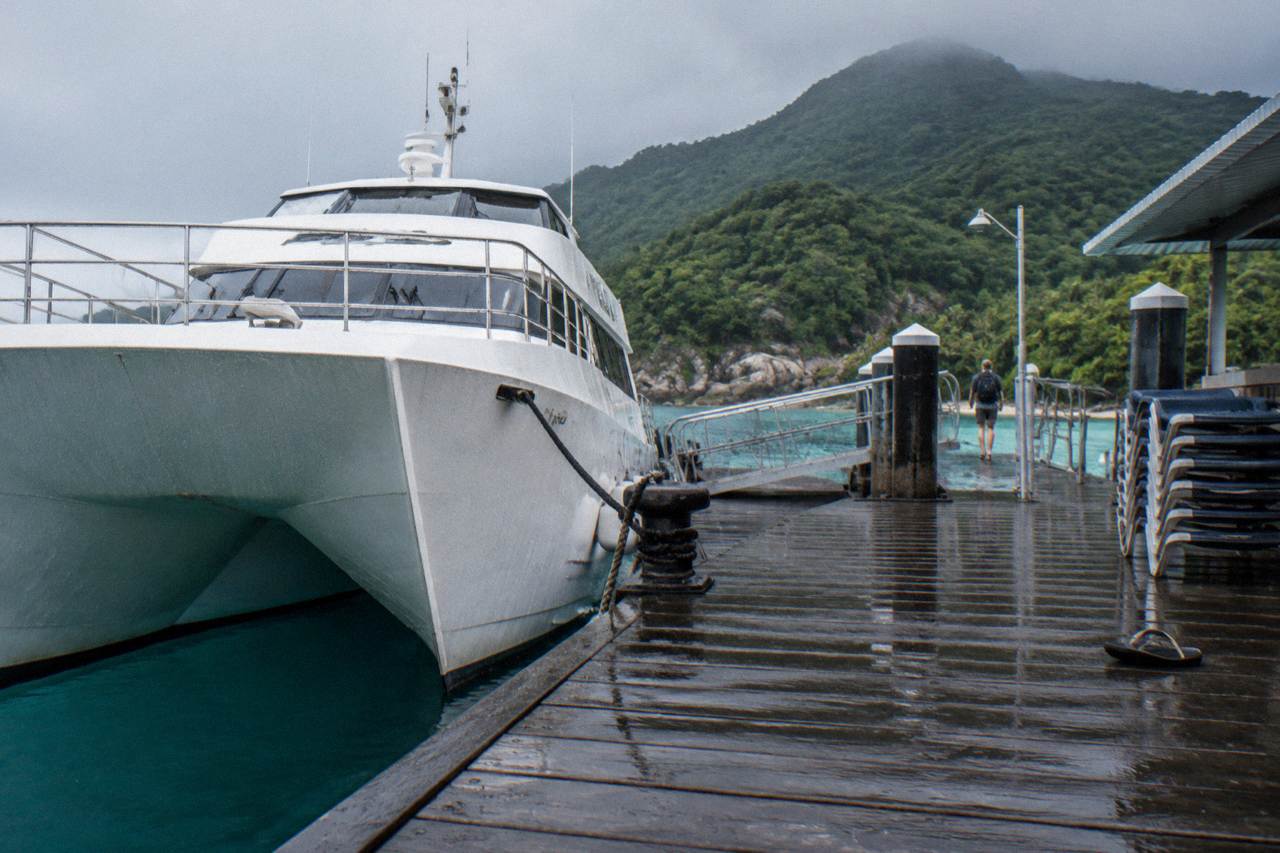 A fast catamaran ferry moored at a tropical island jetty with forested hills behind