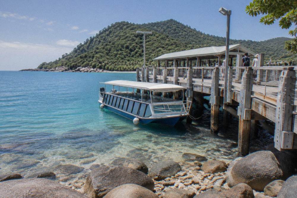 A boat with transparent viewing panels moored near a tropical island jetty