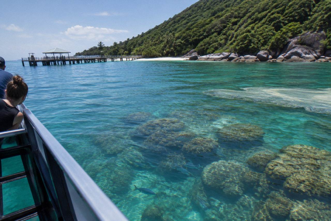 Calm turquoise water over coral reef beside a forested tropical island