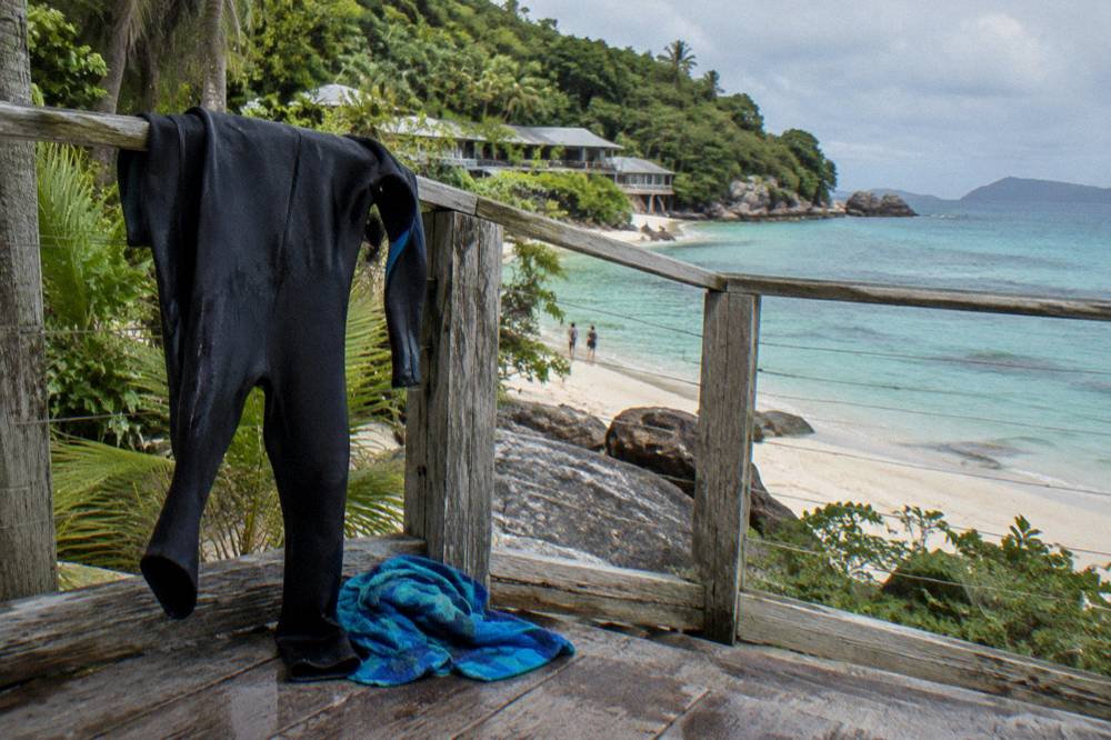 A full body stinger suit drying on a railing beside a beach