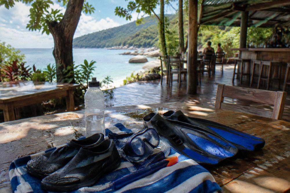 Snorkel mask and fins laid out on a wooden bench beside a towel