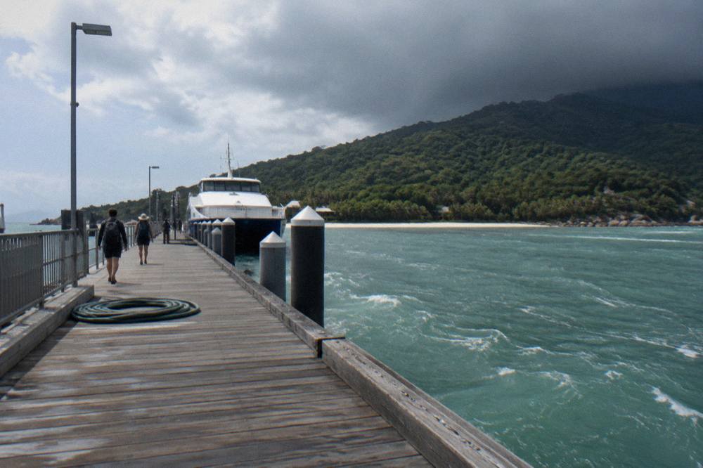 A fast catamaran ferry approaching a jetty in a sheltered tropical bay