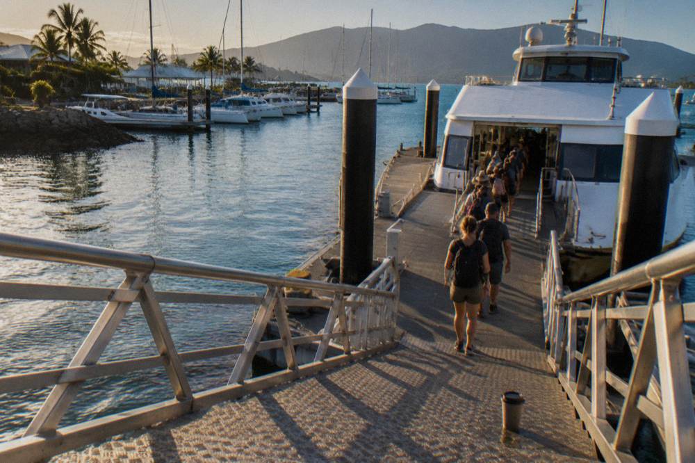 Passengers boarding a white fast ferry at a timber marina jetty in morning light