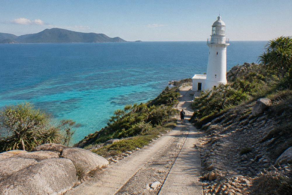 A white lighthouse on a rocky headland above turquoise coral water