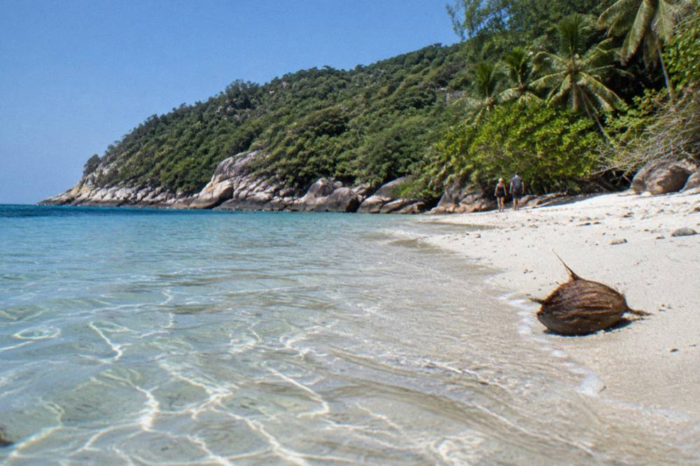 A white sand beach with clear shallow water and headland in the background under a blue sky