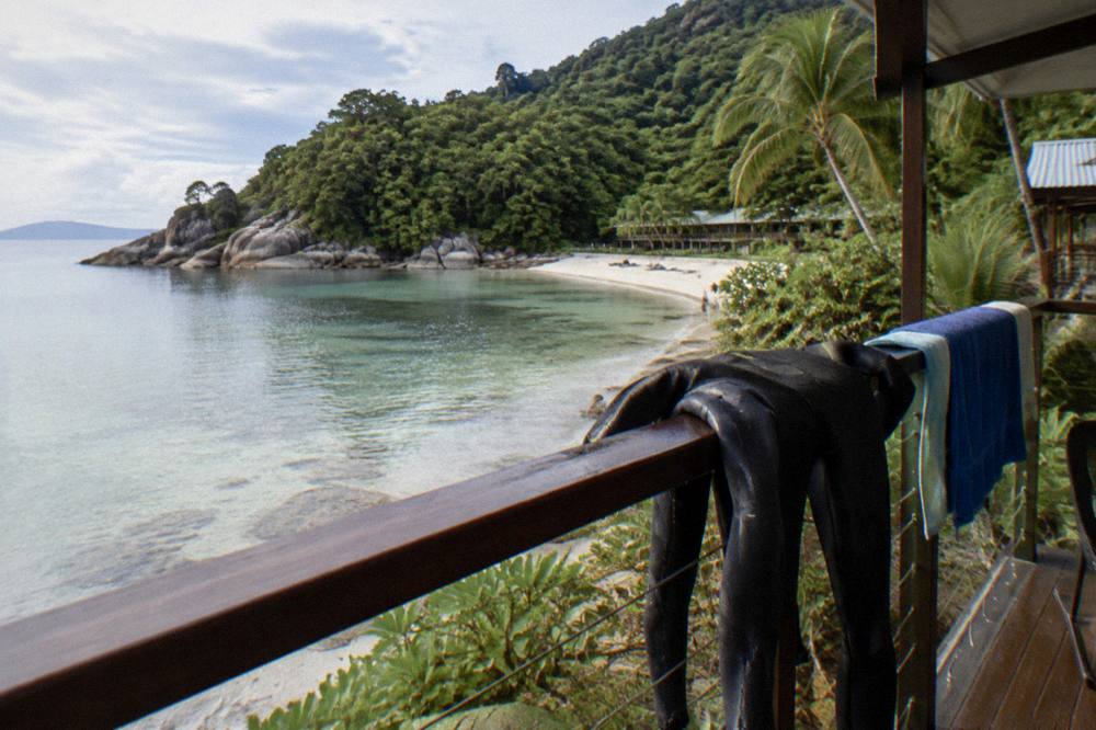 A calm sandy beach with a rocky point and dense green trees at the far end