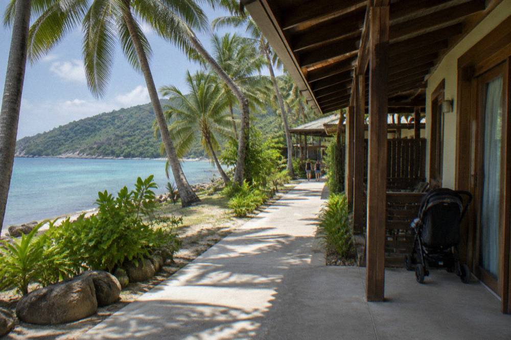Wide flat path along a tropical beachfront with palm trees and timber buildings