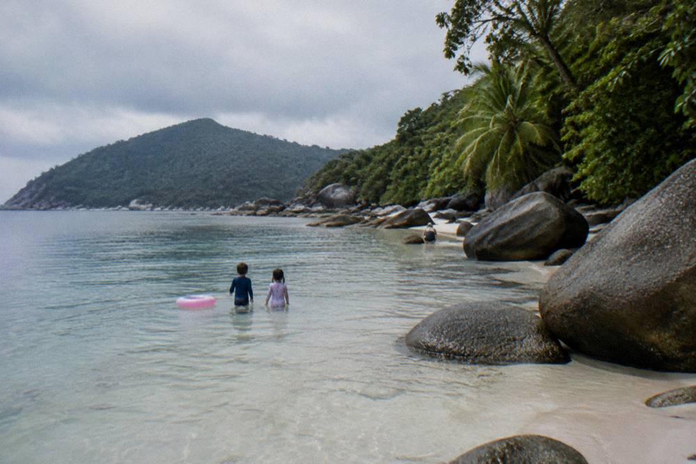 Children's feet standing in clear shallow water above pale coral sand