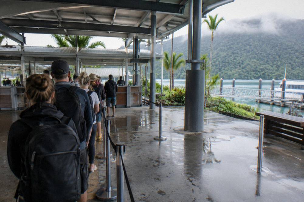 Passengers queueing at an open-air marina terminal counter before boarding