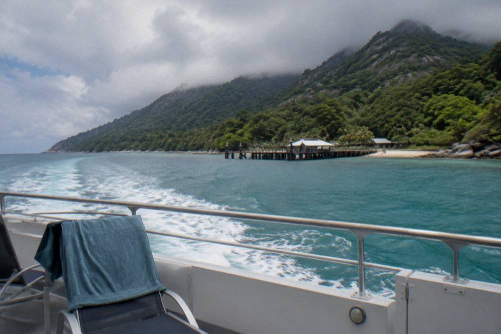 Ferry crossing open water toward a forested tropical island in the distance