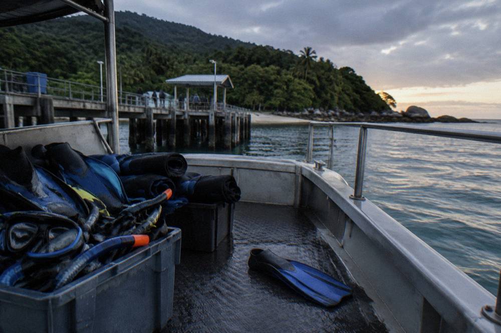 Snorkel fins masks and lycra suits stacked on a boat deck near a jetty