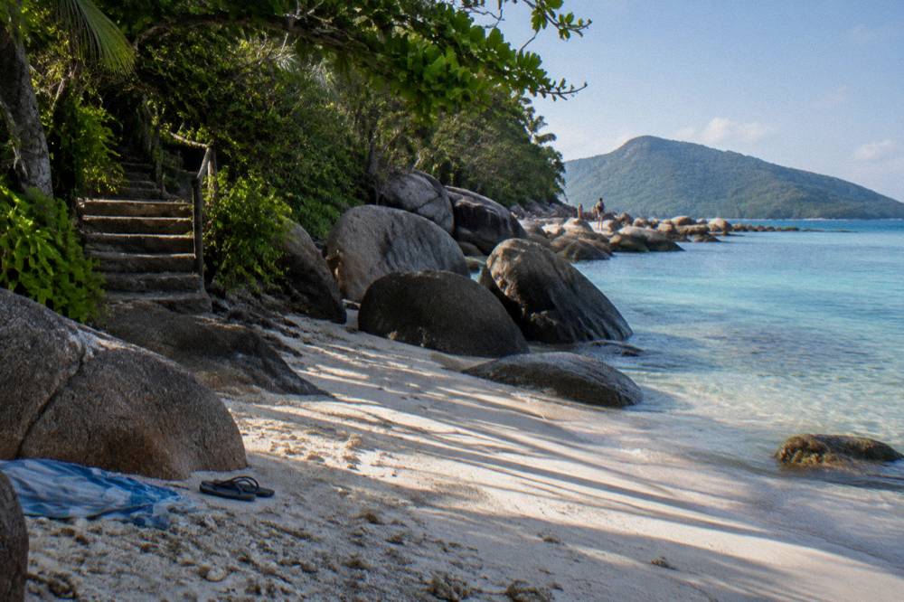 White coral sand beach framed by granite boulders and rainforest at the end of a walking track