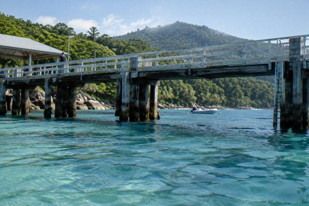 Wooden jetty at a tropical island with anchored boat and dense green headland
