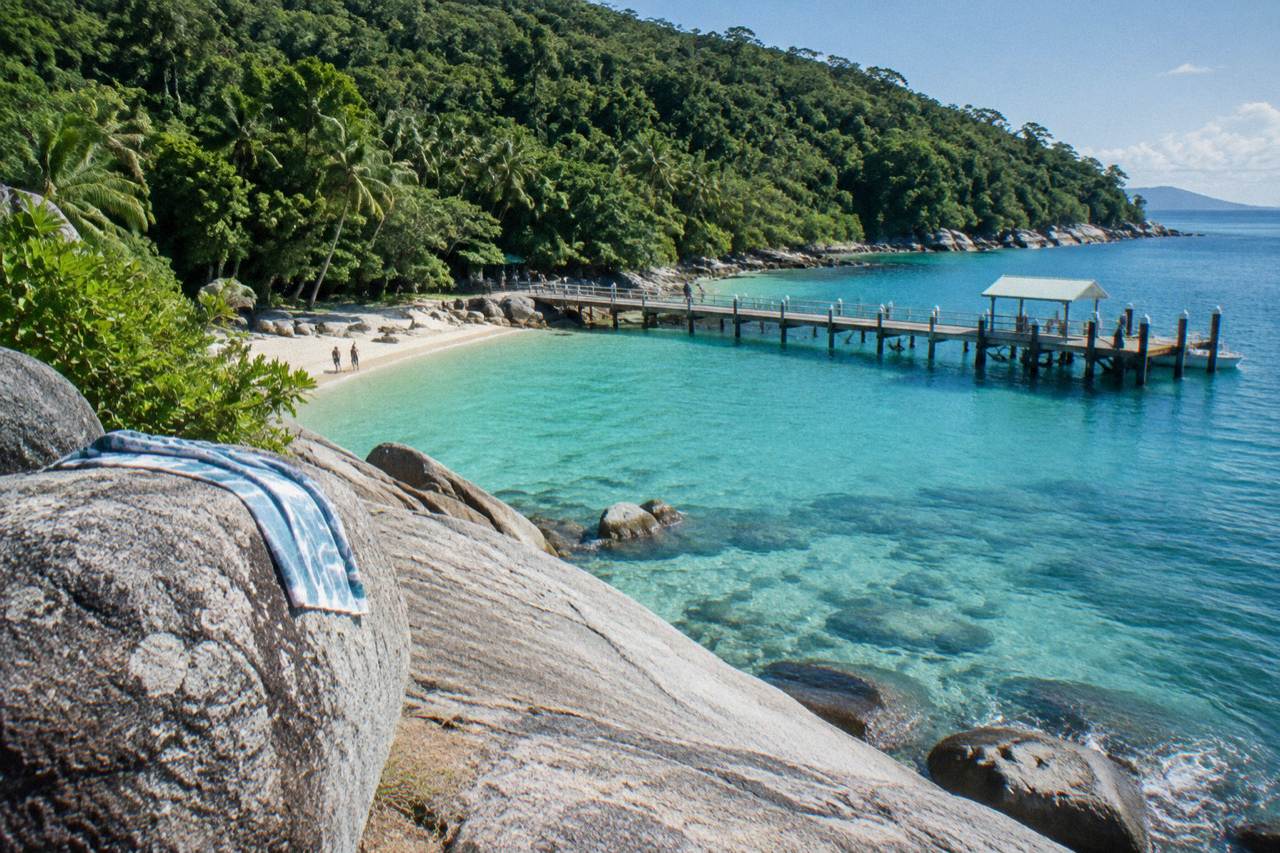 Granite boulders and coral beach at Welcome Bay with calm turquoise water and rainforest behind