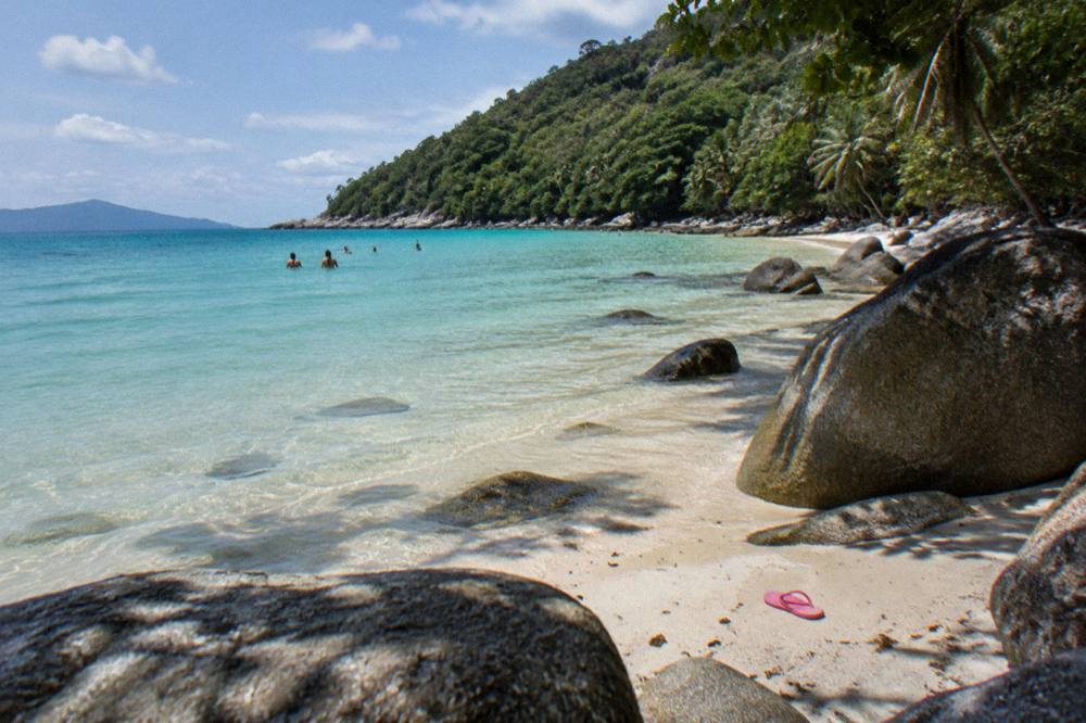 Sheltered tropical beach with calm shallow water and granite boulders along the shoreline